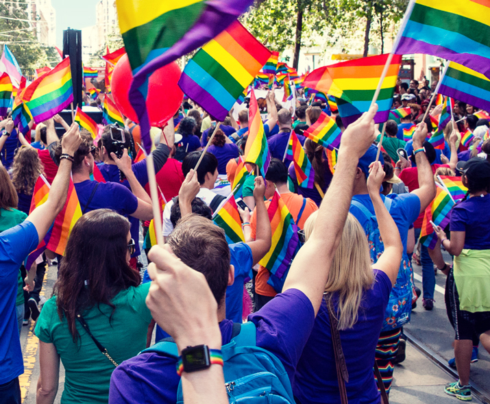 Foto einer Gruppe von Menschen, die auf einer Parade Regenbogenflaggen schwenken.
