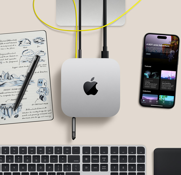 Pohled shora na stříbrný Mac mini, k jehož portům jsou připojené různé kabely a flashová jednotka, v sestavě s bezdrátovou klávesnicí, trackpadem a iPhonem, vedle leží poznámkový blok
